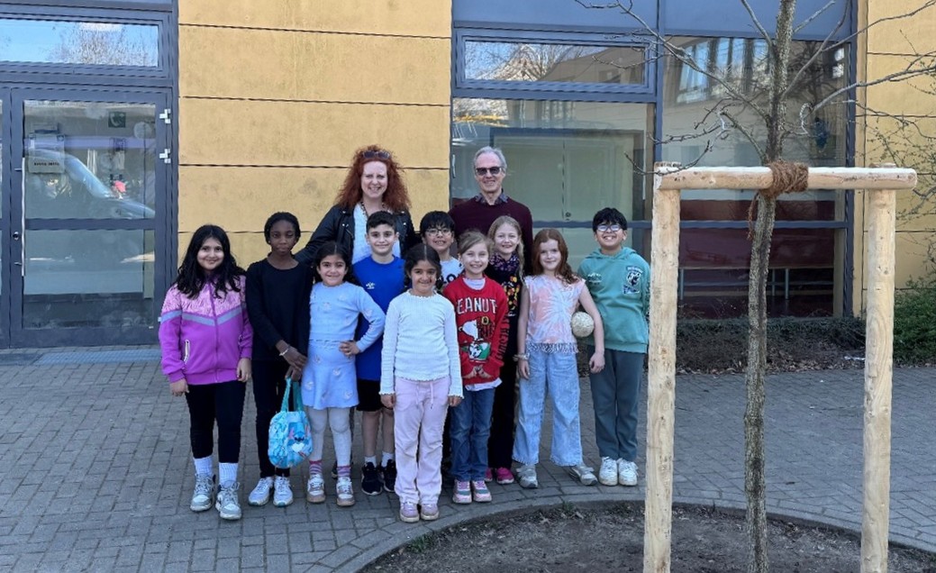 Die Kinder der Projektgruppe der Astrid-Lindgren-Grundschule vor ihrem frisch gepflanzten Amber-Baum.  Stehend: Rektorin Natalie Becker und Dr. Harald Müller-Witt, Lions Club Ratingen.